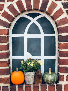 Orange and green pumpkins with flowers on a brick arched windowsill