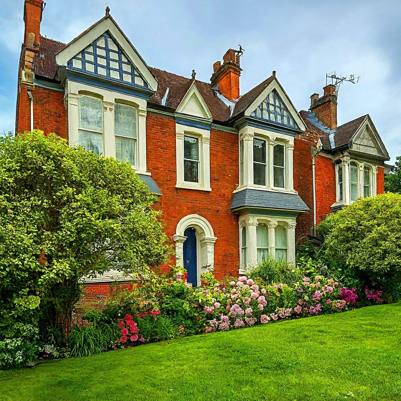 Victorian red brick house with bay windows and colorful garden