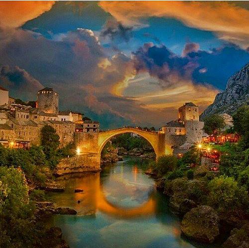 Stone arch bridge over river at sunset with historic buildings and colorful sky