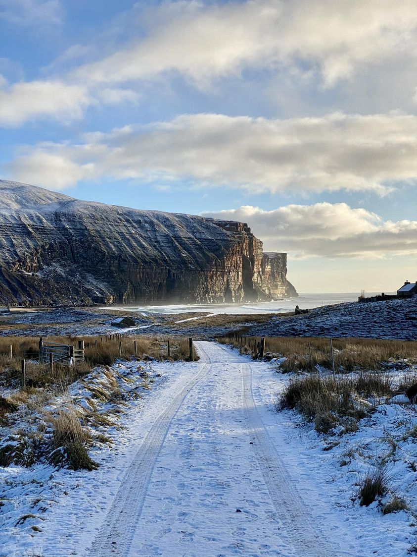 Snowy path toward tall coastal cliffs on Hoy island, Scotland with cloudy sky