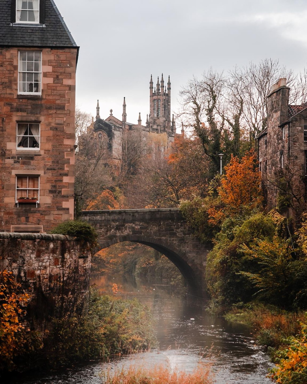 Historic stone buildings and arched bridge over a river in Edinburgh, Scotland, with autumn trees