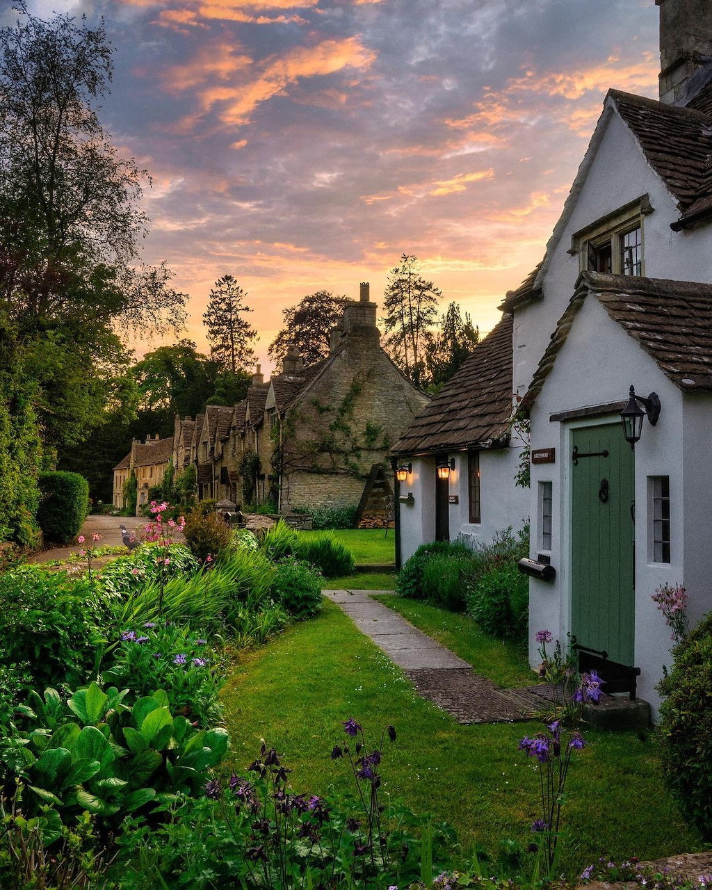Traditional English stone cottages with green garden path and dramatic sunset sky