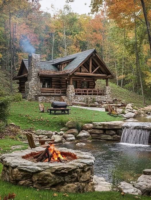 Log cabin by pond with waterfall and campfire in autumn forest