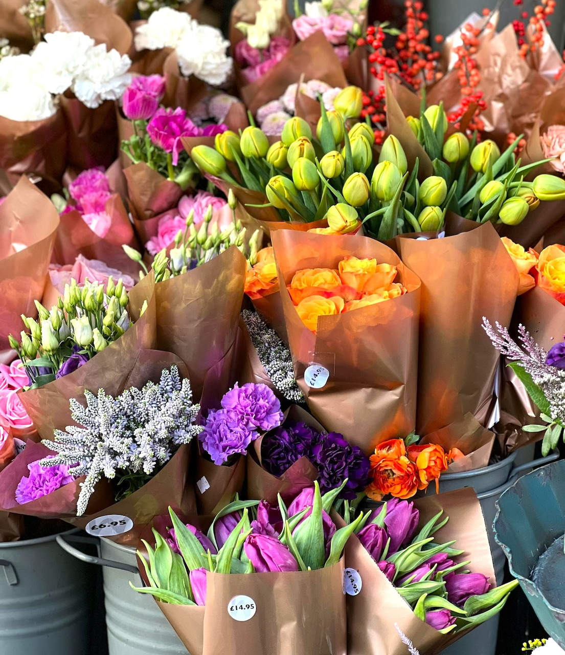 Vibrant flower bouquets in paper wrapping displayed at a flower shop with tulips, roses and various colorful blooms
