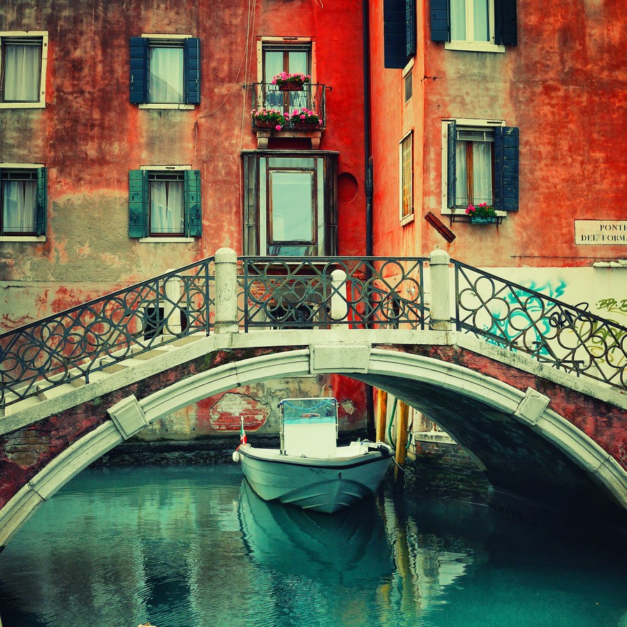 White boat under decorative bridge in Venetian canal with orange buildings