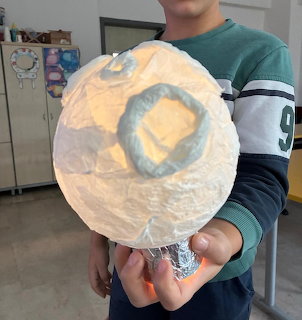 Child holding a handmade white paper ball lantern that glows orange from within, indoors