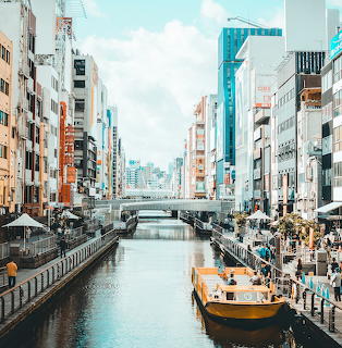Dotonbori canal in Osaka with buildings, bridges, yellow boat and people along waterfront