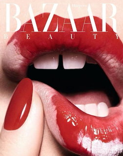 Close-up of glossy red lips with teeth showing and a finger with red nail polish touching the lower lip