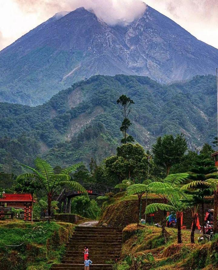 Large volcanic mountain peak with dense forest and stone stairway leading up through tropical vegetation