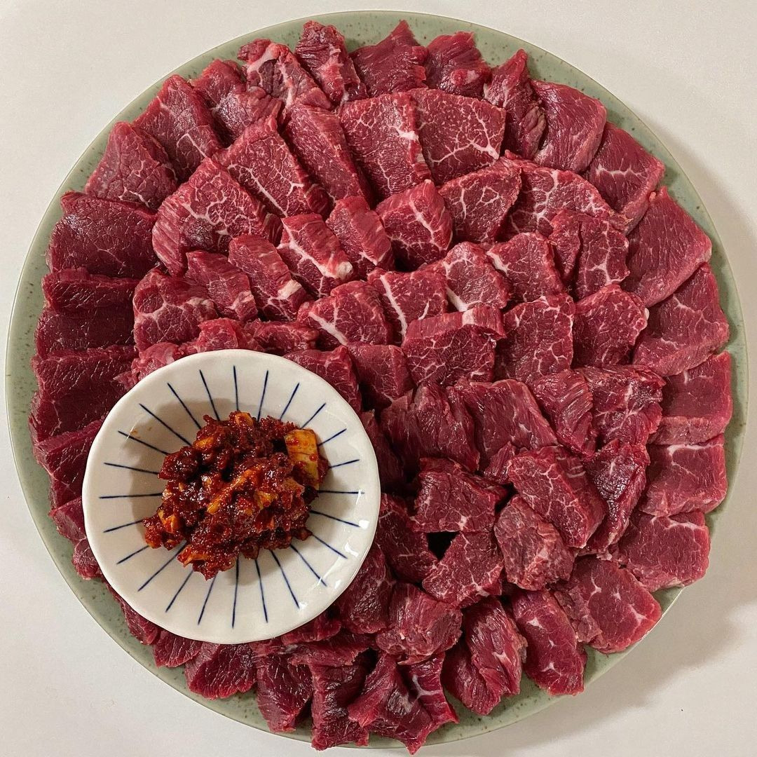 Sliced raw beef on a round plate with a small bowl of red chili sauce