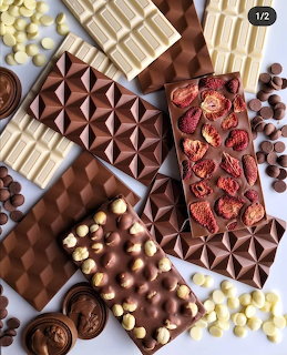 Assorted chocolate bars with nuts, fruit, and candy toppings arranged on white background