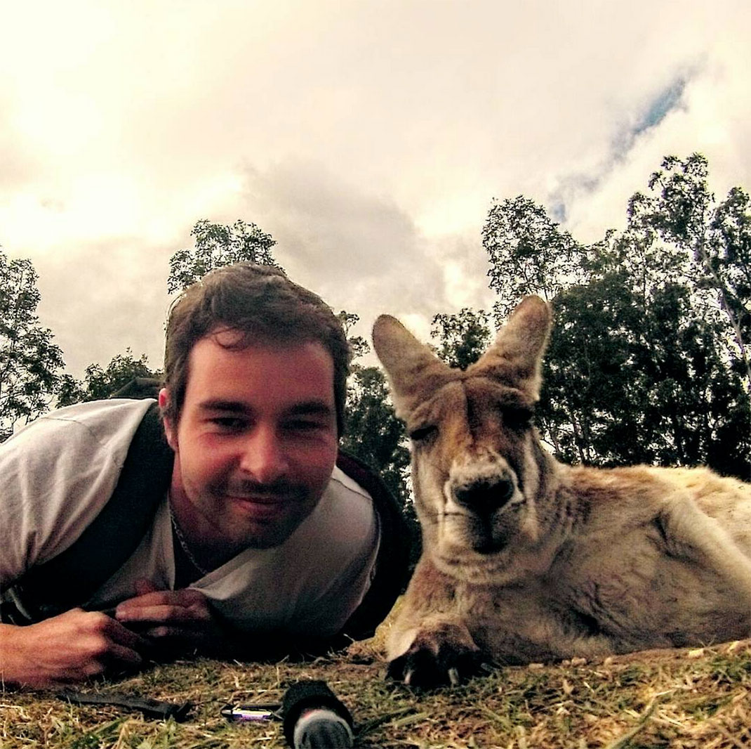 Man lying next to a kangaroo on grass outdoors with trees behind them