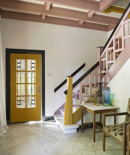 Art deco interior with pink staircase, exposed beams, yellow door with geometric glass, and console table