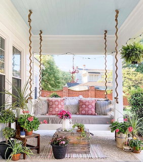 White porch swing with coral pillows and plants on covered veranda