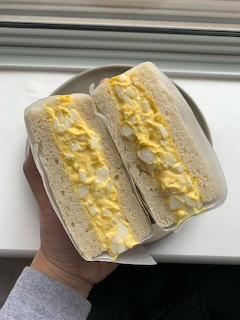 Hand holding plate with two egg sandwiches filled with yellow scrambled eggs