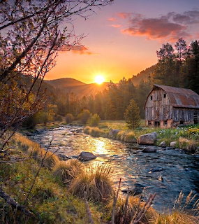 Old barn by mountain stream at sunset with golden light and colorful sky