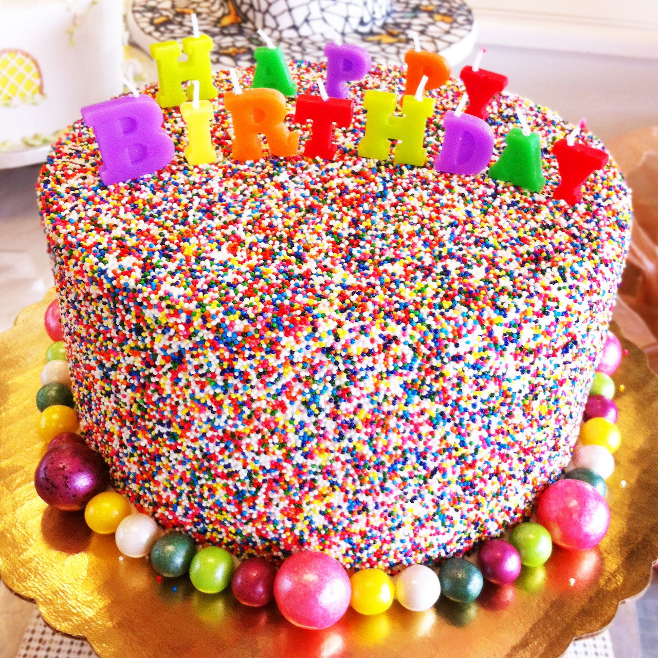 Birthday cake covered in multicolor sprinkles with Happy Birthday letter candles and candy pearl border