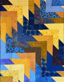 Geometric quilt featuring blue and gold arrow blocks in diagonal arrangement