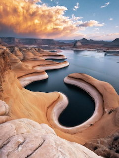 Blue lake winding through smooth sandstone canyon formations beneath glowing clouds