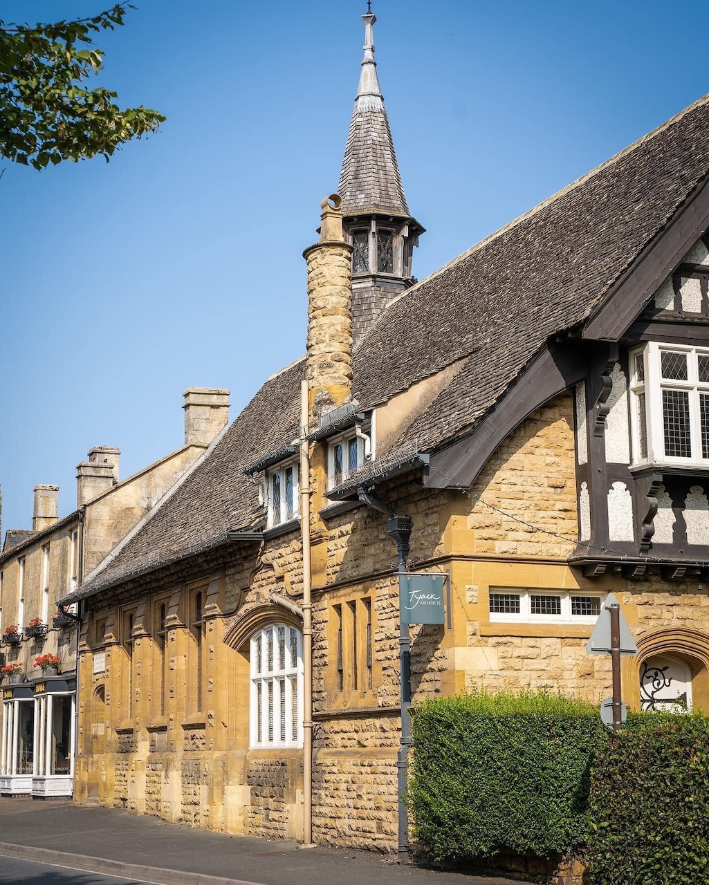 Row of golden stone cottages with thatched roofs and church tower in Cotswold village