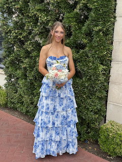 Woman in a blue floral formal gown holding a bouquet in front of a hedge