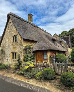 Traditional stone cottage with thatched roof and garden under blue sky