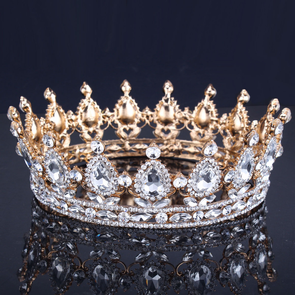 Ornate gold crown with clear gemstones and pearls on black reflective surface
