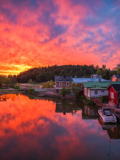 Vibrant sunset reflecting over red wooden buildings along a calm Finnish harbor with dramatic pink and orange clouds
