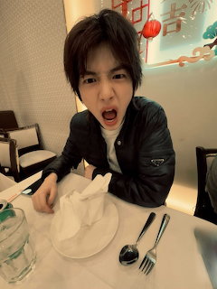 Young man in black jacket making a playful angry expression at a restaurant table with utensils