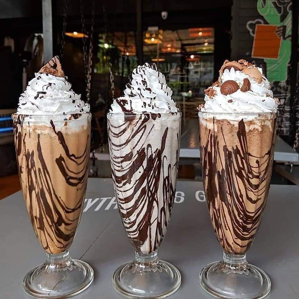 Three chocolate milkshakes with whipped cream and chocolate drizzle in tall glasses
