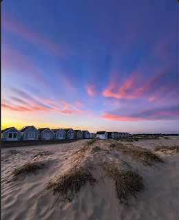 Row of beach huts on sandy dunes under a colorful pink and blue sunset sky at Mudeford Sandbanks