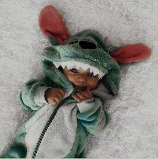 Baby lying on a fluffy white blanket wearing a green dinosaur onesie