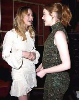 Two women in formal dresses talking and smiling at an indoor event