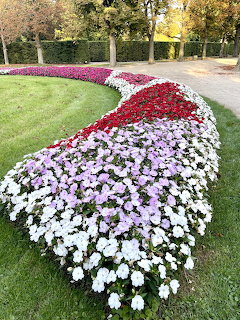 Winding flower bed with white, pink and red flowers on green lawn in formal garden