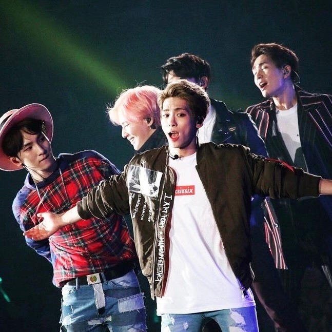 Five SHINee members performing on stage in colorful concert outfits