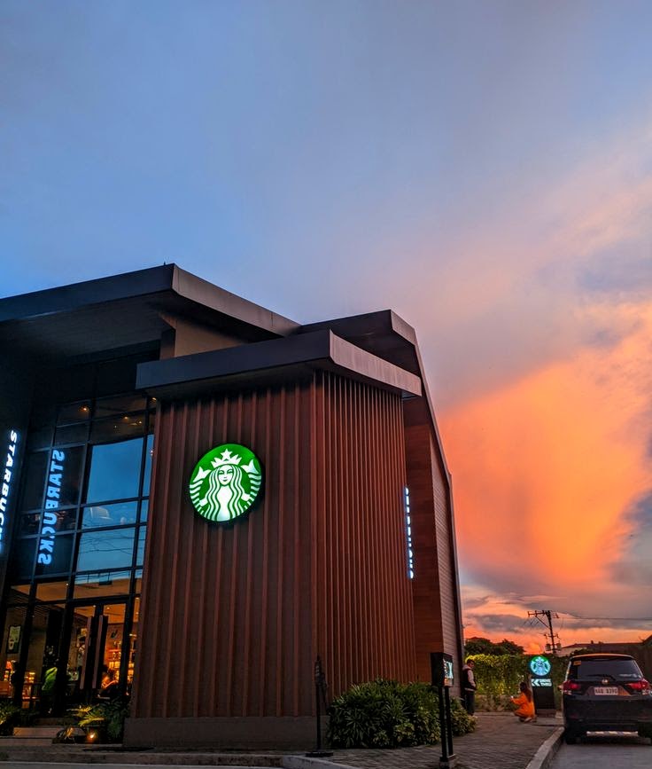 Starbucks exterior building with glowing green logo under a vibrant orange and blue sunset sky