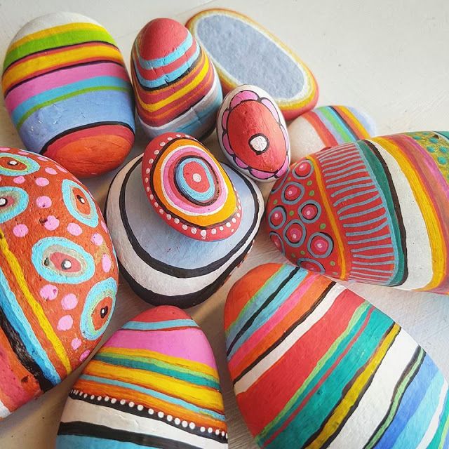 Collection of smooth stones painted with vibrant rainbow stripes, circles, and geometric patterns
