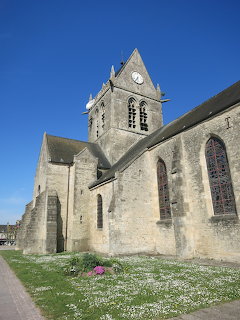 Historic stone church with bell tower and Gothic windows under blue sky in Normandy