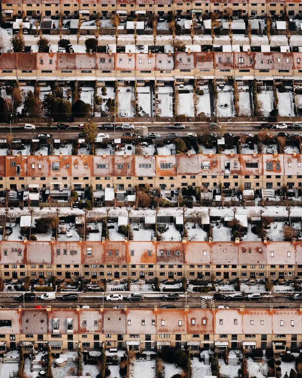Aerial top-down view of rows of orange-toned apartment buildings with snow-covered rooftops and parked cars