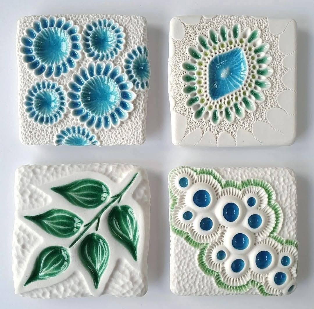 Four square ceramic tiles with blue and green botanical patterns on white textured backgrounds