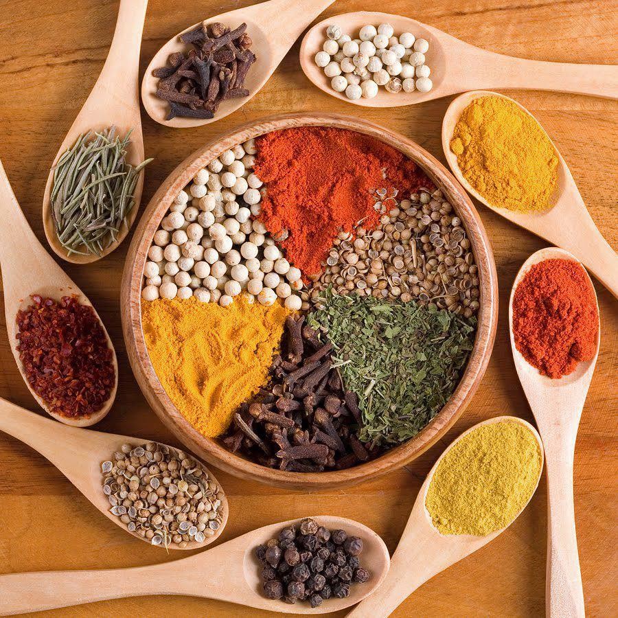 Assorted colorful spices and herbs in wooden bowl and spoons on wooden table