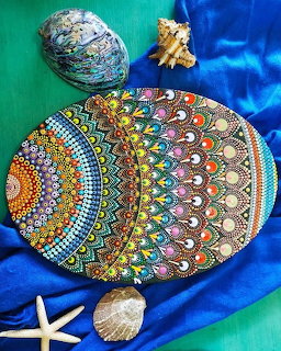 Colorful elliptical mandala with dotted concentric patterns surrounded by seashells on blue and green fabric