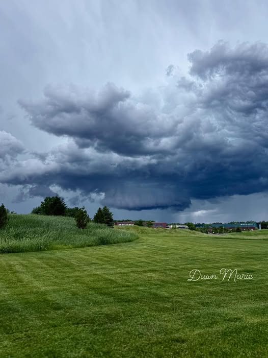 Dark storm clouds forming over a lush green field with distant buildings in Sheboygan, Wisconsin