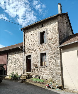 Old stone house with green shutters and a brown door on a village street under blue sky