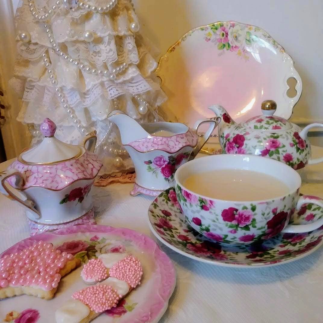 Vintage floral tea set with a cup of tea and pink heart-shaped cookies on a lace table