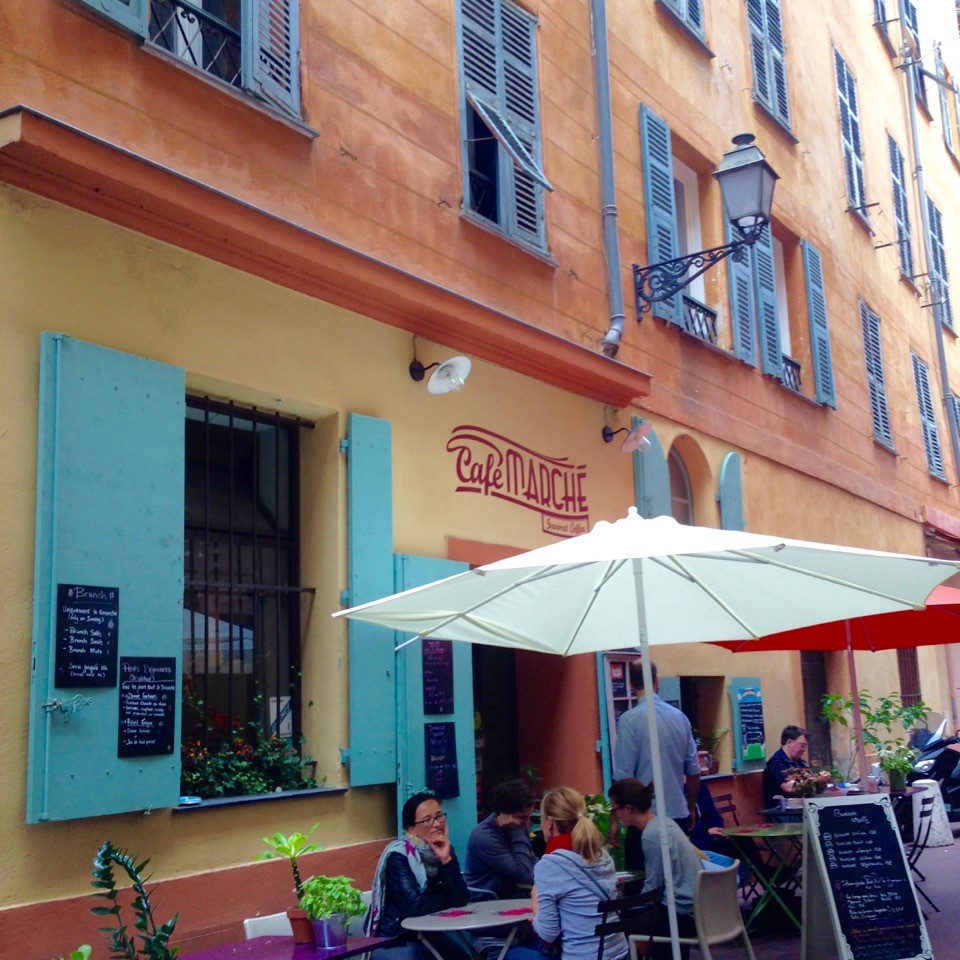 Orange buildings with blue shutters and outdoor cafe seating with white umbrellas in Nice, France