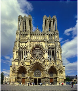 Front facade of Reims Cathedral with Gothic spires, rose window, and arched portals against a cloudy blue sky