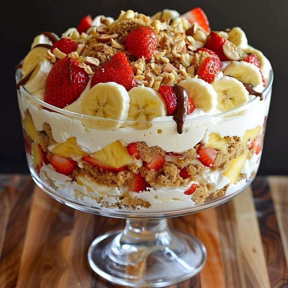 Layered trifle with strawberries, bananas, whipped cream and nuts in glass pedestal bowl