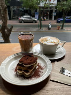 Two coffee cups with latte art and tiramisu cake on table at café with street view