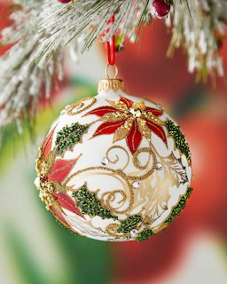 Red and white glass Christmas ornament with poinsettia design hanging from frosted evergreen branch